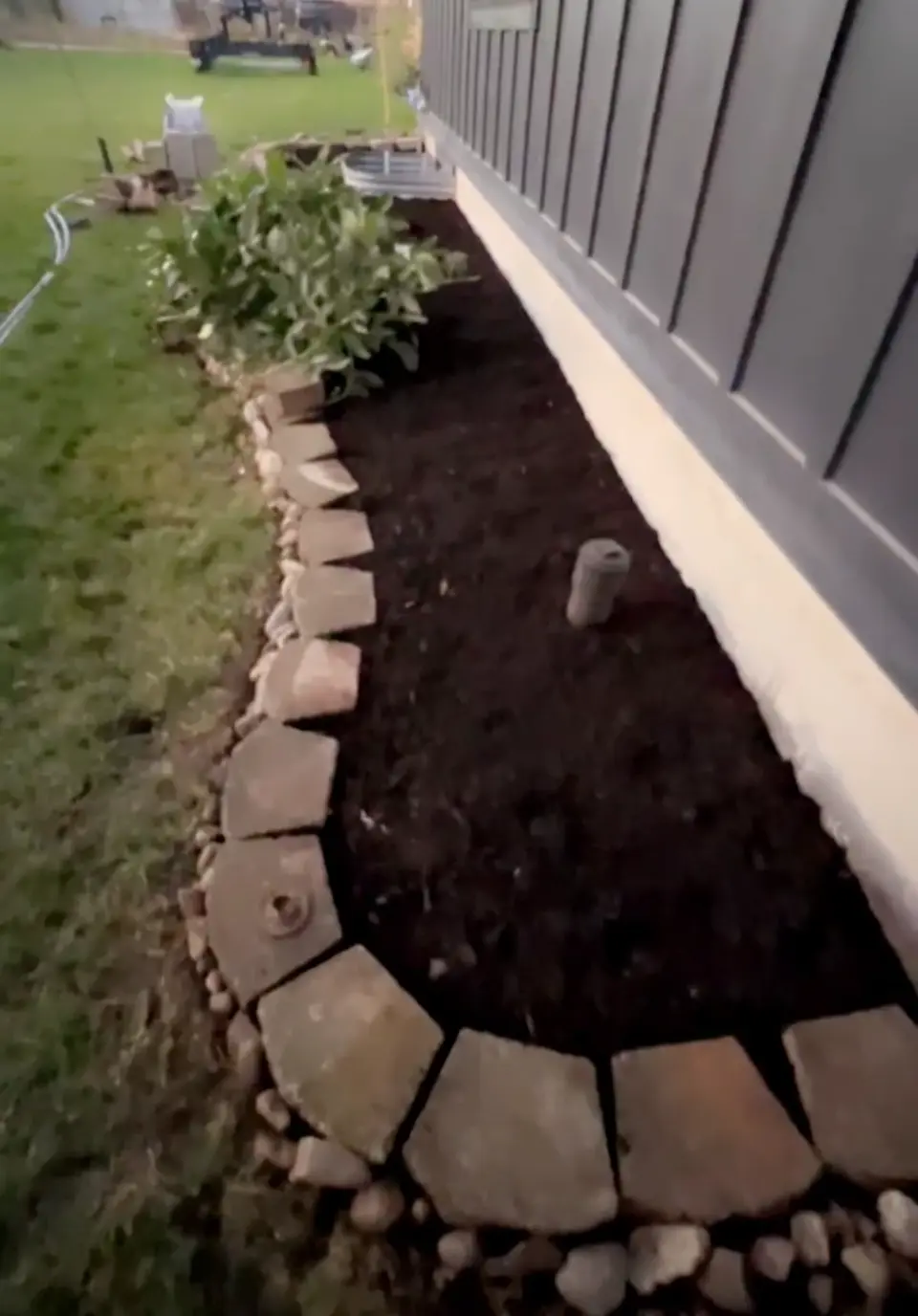 New flower bed with fresh mulch and a stone border along a house